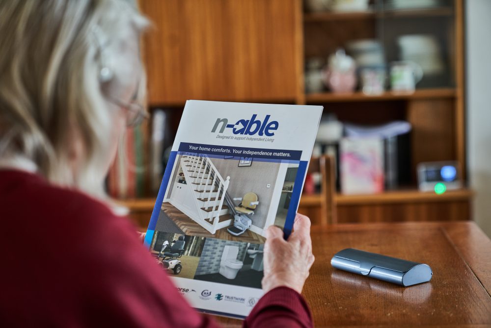 n-able brochure Older woman reading an N Able stairlift brochure at home